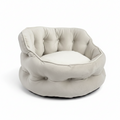 A tufted round pet bed in a light cream or off-white fabric, shown from the front on a white circular base against a solid green background.