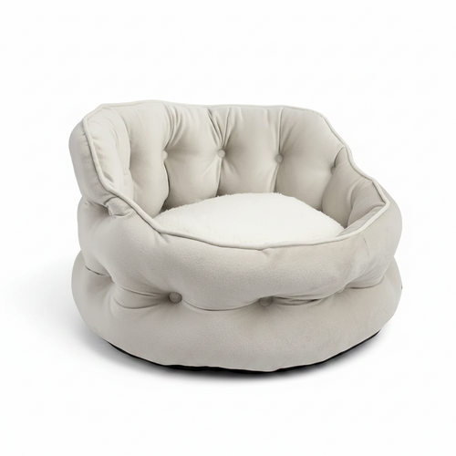 A tufted round pet bed in a light cream or off-white fabric, shown from the front on a white circular base against a solid green background.
